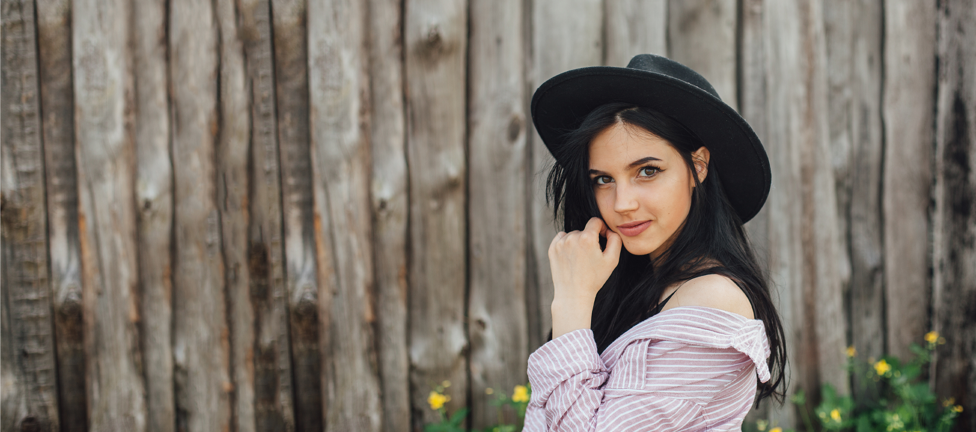 young confident woman standing in front of a rustic wood fence